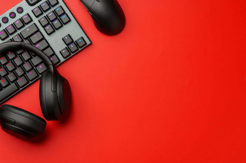 Computer keyboard and headphones on red background top view